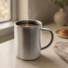 A stainless steel coffee mug with steam rising from the hot beverage inside, placed on a countertop.