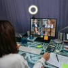 A workspace with a person in front of a computer displaying a video call, featuring a ring light and various office supplies.