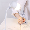 A white wireless charging sound lamp with a curved neck and glowing bulb sits on a desk beside a person writing.