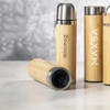 A drink bottle with a bamboo exterior and stainless steel lid, featuring a logo. Several similar bottles are in view.