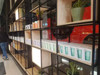 A display of Ecco Kuppa Universal reusable coffee cups, featuring various colours, arranged on shelving alongside plants.