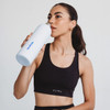A drink bottle with a white body and metallic cap, held by a person wearing a black sports top, featuring a logo.