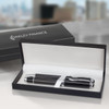 A sleek black pen with silver accents inside a black presentation box, featuring a logo on the lid.