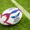 A white touch rugby ball with red and blue accents, featuring a logo on the surface, set on grass.