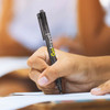 A black plastic pen with a logo, being held while writing on paper.