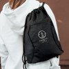 A black drawstring backpack is worn on a person's back, featuring a logo and a zippered pocket.