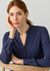 A woman poses wearing a navy long sleeve blouse with a button-up neckline, sitting against a light background.