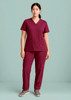 A woman stands wearing burgundy straight leg scrub pants and a matching short-sleeve top. The outfit has two pockets.