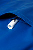 A close-up of a blue scrub top featuring a white zippered pocket. It has a logo visible on the fabric.