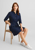 A navy blue women's dress with a belted waist, collared neckline, and two front pockets, paired with white sneakers.