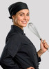 A chef in a black uniform and black bandana holds a whisk, smiling against a grey background.