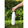 A drink bottle in white with a metal loop, designed for easy carrying, set against greenery.
