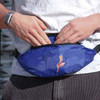 A blue bum bag featuring a floral design, being worn by a person with hands adjusting it.