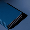 A navy blue hardcover notebook with a subtle logo, featuring multiple stacked layers on a dark background.