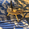 A round bamboo picnic table with drink holders, set on a striped blanket, accompanied by wine glasses and a cheese board.