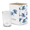 A stackable clear glass tumbler next to a decorative box featuring a floral design and a logo.