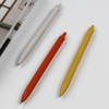 Three plastic pens in white, orange, and yellow, arranged on a flat surface next to a book. Each pen features a logo.
