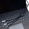 A black charging cable with multiple connectors lies on a laptop keyboard. The cable features a circular connector with branding.