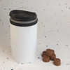 A reusable white coffee cup with a black lid, accompanied by several brown chocolate cups.