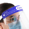 A clear protective face shield with a blue top band and a warning label, worn by an individual with glasses and a mask.