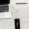 A square-shaped wheat straw charging cable in beige connects a phone to a laptop on a marble surface.