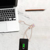 A wheat straw charging cable in a man shape, in beige, connected to a smartphone and a laptop on a marble surface.