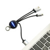 A round-shaped light-up charging cable with multiple connectors, featuring a keyring attachment, displayed near a laptop.