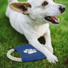 A rope Frisbee dog toy in navy blue sits on the grass next to a happy dog, featuring a paw print design.