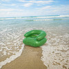 A green custom inflatable chair situated on a sandy beach with gentle waves in the background.