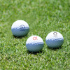 A set of three white golf balls, featuring logos, resting on green grass.