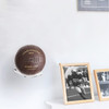 A vintage brown soccer ball displayed on a wall shelf, alongside framed photographs. The ball features a logo.