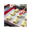 A silicone baking mat in red is placed on a baking tray, with savoury pastries being brushed with a red tool.