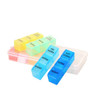 A set of colourful pill organisers in blue, yellow, and pink, housed in a clear container, featuring compartments for days and times.