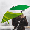 A green and white umbrella with a logo, held by a person with their back turned, against a misty background.
