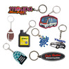 A collection of custom-shaped PVC keyrings in various designs and colours, including a football, oil can, and police car.