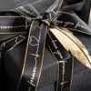 A black ribbon with gold edges, featuring a heartbeat design and text, tied around a dark gift box.