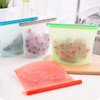 Silicone reusable storage pouches in green, clear, and red, displayed on a kitchen countertop. They feature zip closures and various contents.