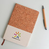 A natural cork and cotton A5 notebook with a logo, accompanied by a wooden pen on a light background.