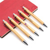 Five eco bamboo pens with silver accents are arranged next to a red notebook, featuring a logo on the pens.