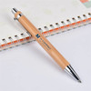 A bamboo pen with a silver clip rests on a lined notebook, featuring a logo on its barrel.