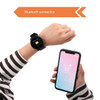 A round black smart watch on a wrist, paired with a smartphone displaying weather information.