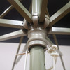 A close-up of a green patio umbrella's support structure and pulley system, featuring a central joint and connecting ropes.