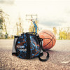 A ball backpack in black and blue with a logo, resting on a basketball court next to a basketball.