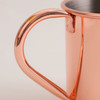 A copper mug with a curved handle, exhibiting a shiny metallic finish and smooth texture.