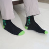 Black and green bamboo socks displayed on a person's feet, featuring a logo on the side.