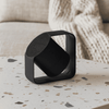 A black wireless speaker with a unique design sits on a speckled table, surrounded by a soft, textured background.