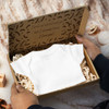 A die cut box with a locking lid, featuring a white onesie and decorative filling, displayed in hands.