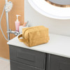 A yellow Kraft paper cosmetic bag with a zip closure, resting on a countertop. It has a handle and a logo.