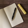 A metal pen rests on an open notebook with dotted pages, alongside a yellow highlighter.