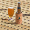A drink bottle in a cork stubby holder with base, accompanied by a glass of beer on a wooden surface.
